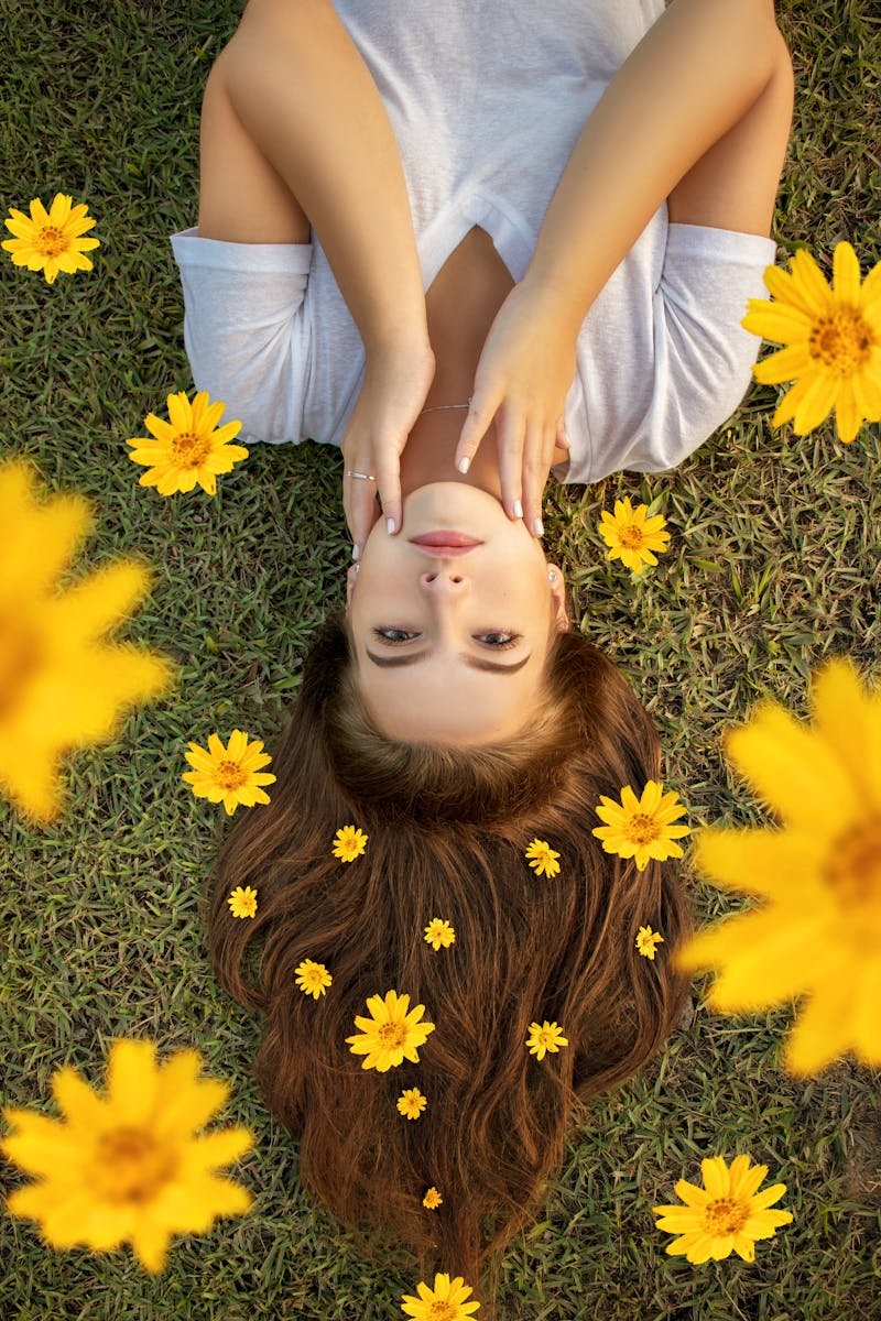 Upside down portrait of a woman lying on grass with yellow flowers in her hair.