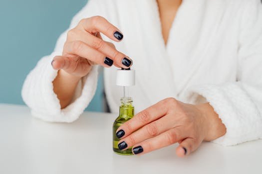 Close-up of a woman in a white bathrobe using a skincare product dropper with painted nails.